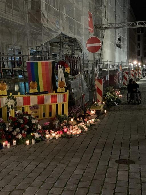 An der Straßenecke an der Schlossstraße, mitten in der Dresdener Innenstadt zwischen Kulturpalast und Residenzschloss, wo ein schwules Paar angegriffen und einer der beiden Männer getötet wurde, erinnern Blumenkränze und Kerzen an die Opfer. Inzwischen hat jemand dort auch eine Regenbogenfahne befestigt.