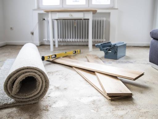 Ein Raum, der renoviert wird. Holzlatten, Teppiche und Arbeitsmaterialien von Handwerkern liegen auf dem Boden.