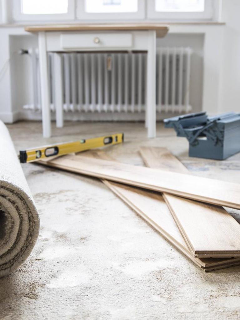Ein Raum, der renoviert wird. Holzlatten, Teppiche und Arbeitsmaterialien von Handwerkern liegen auf dem Boden.