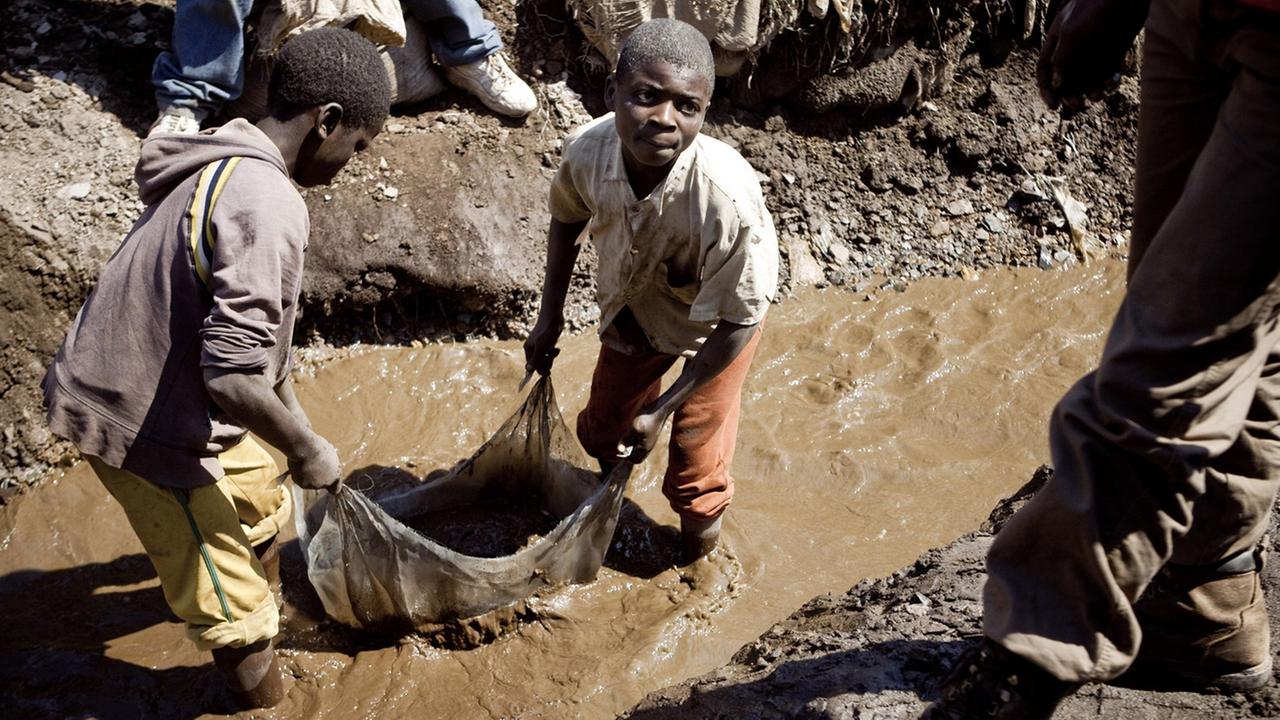 Kinder, die in einer Kupfermine in der Republik Kongo arbeiten. Sie stehen bis zu den Knien im Schlamm