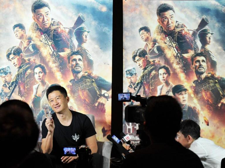 Wu Jing vor Filmplakaten zu Wolf Warrior 2. Im Vordergrund Journalisten mit Kameras und Mikrofonen.