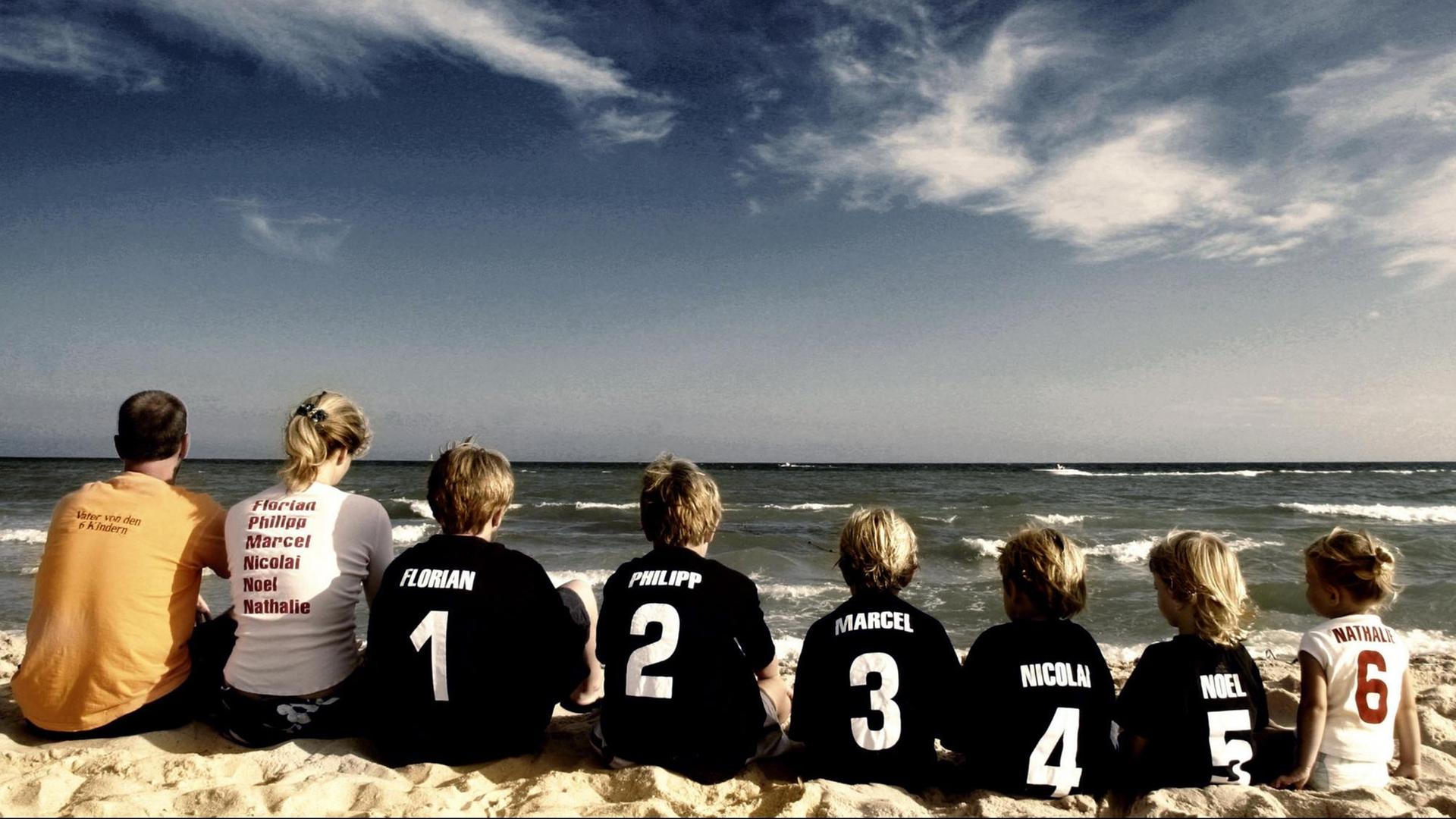 Ehepaar sitzt in einer Reihe mit seinen sechs Kindern am Strand.