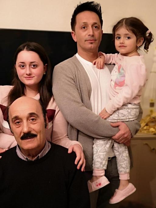 Das Foto zeigt die jesidische Familie Kizilyel in ihrem Wohnzimmer: Im Bildvordergrund sitzt Vater Behcet Kizilyel, dahinter rechts im Bild sein Sohn Salhattin sowie sein Enkelkind und zwei weibliche Familienmitglieder. Kizilyel lebt seit 50 Jahren in Celle.