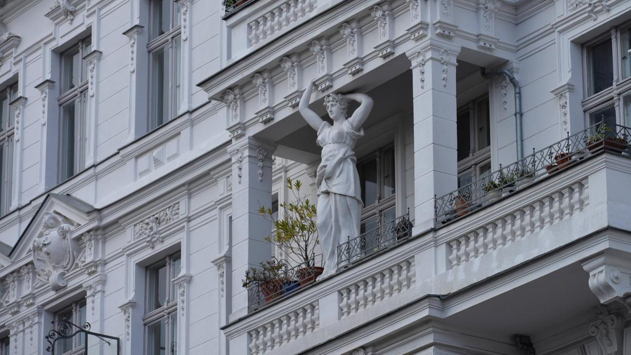 Blick auf eine verzierte Altbaufassade mit Balkon, auf dem eine Frauenfigur als Stützpfeiler zu sehen ist