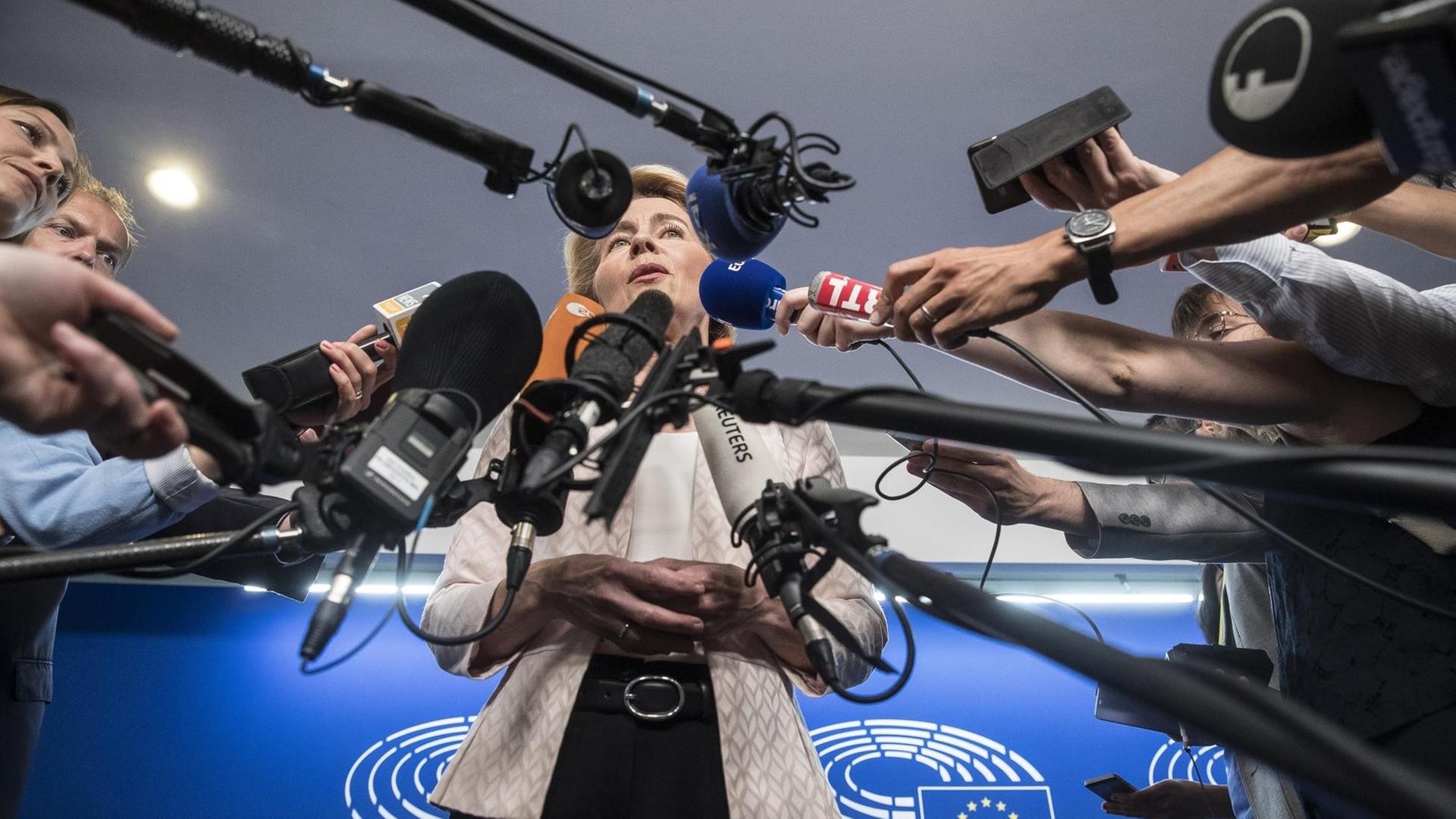 Das Foto zeigt Ursula von der Leyen. Sie beantwortet vor vielen Mikrofonen die Fragen von Reportern im Europäischen Parlament in Straßburg.