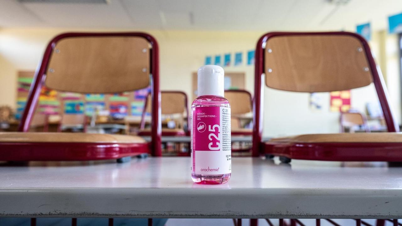 Blick in ein leeres Klassenzimmer. Auf einem Tisch steht Desinfektionsmittel. 