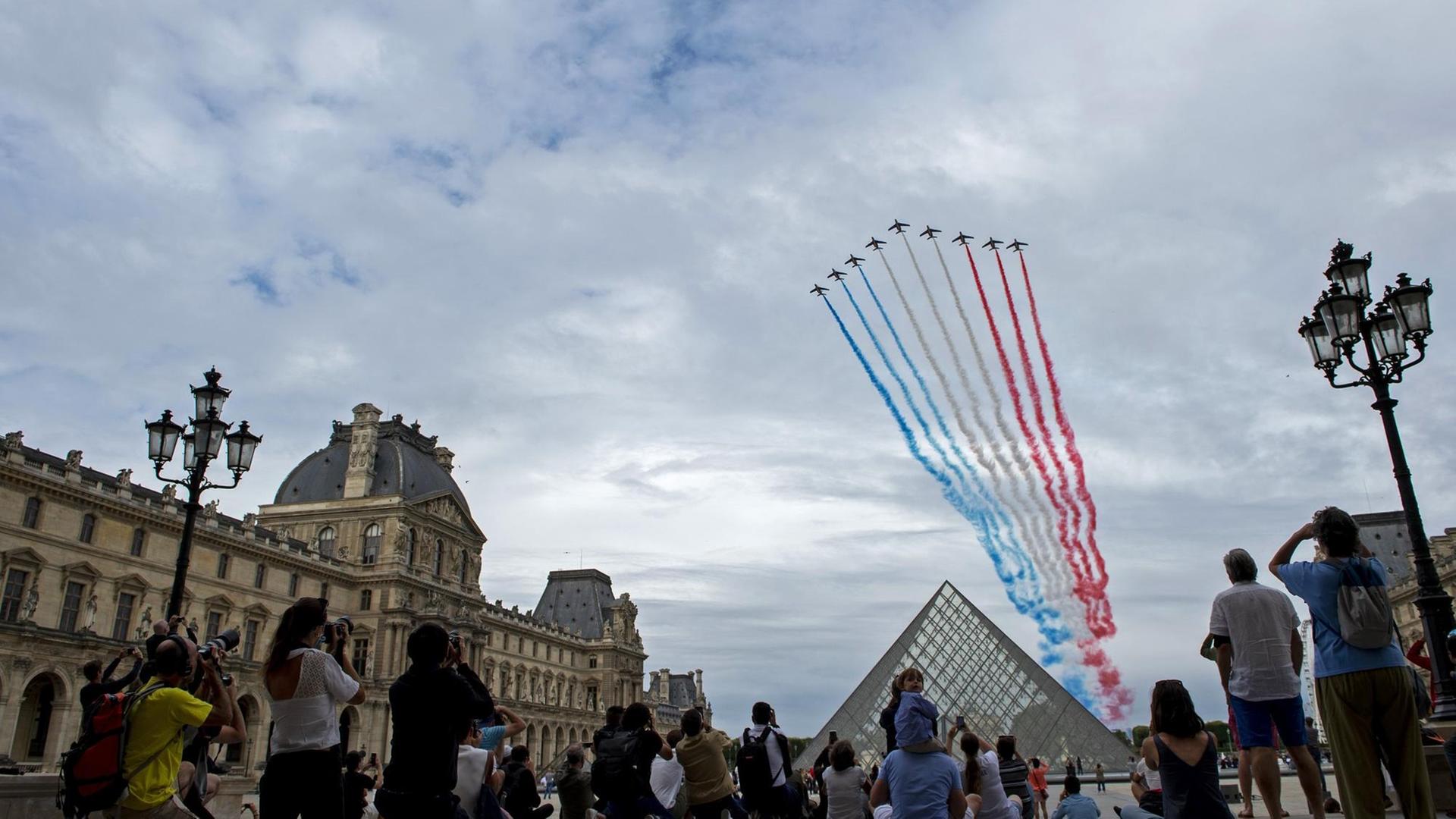 Menschen schauen sich die Düsenjet-Performance am Nationalfeiertag auf dem Platz des Louvre an.