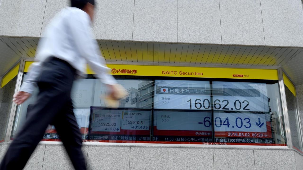 Ein Geschäftsmann läuft an einer Börsenkursanzeige in Tokio vorbei.