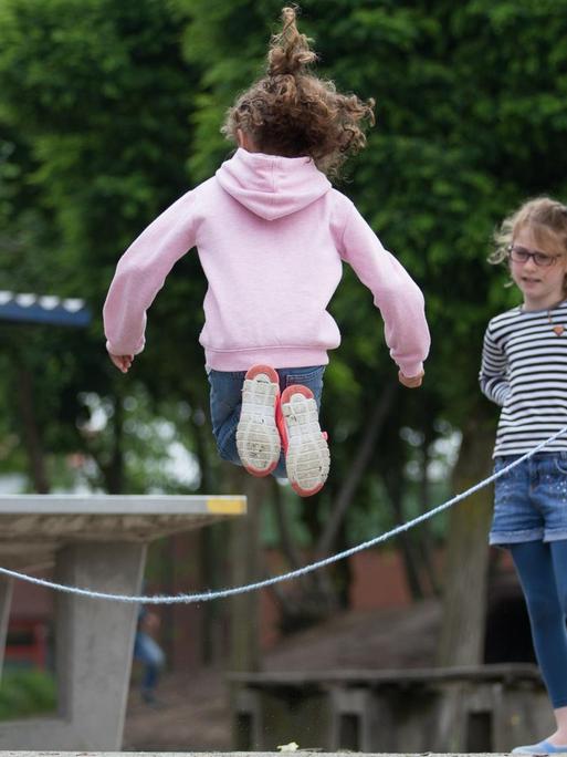 Auf dem Pausenhof einer Grundschule springen Schüler Seil.