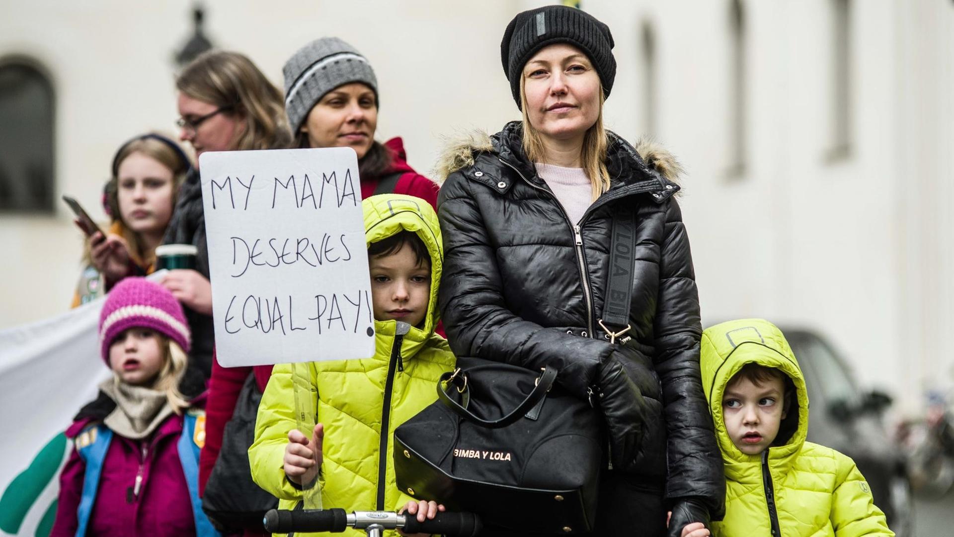 Frauen und Kinder demonstrieren in München für eine bessere Bezahlung von Frauen. Sie halten ein Schild mit der Aufschrift "My Mama deserves equal pay" hoch.