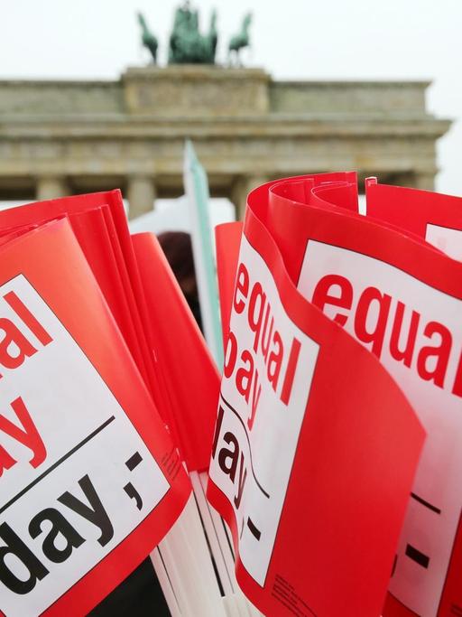 Rote Winkfähnchen mit der Aufschrift "Equal Pay Day", im Hintergrund das Brandenburger Tor in Berlin.