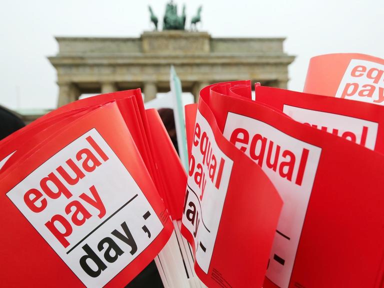 Rote Winkfähnchen mit der Aufschrift "Equal Pay Day", im Hintergrund das Brandenburger Tor in Berlin.