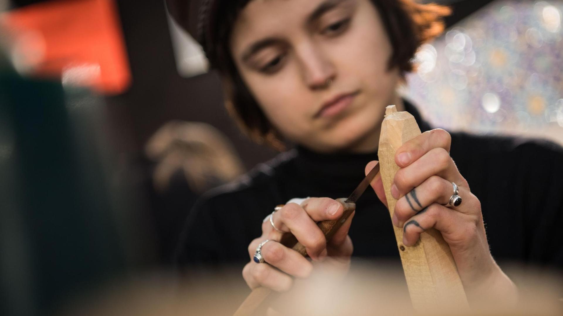 Eine Auszubildende zur Holzbildhauermeisterin bearbeitet auf der Internationalen Handwerksmesse 2018 ein Stück Holz mit einem Schnitzmesser.