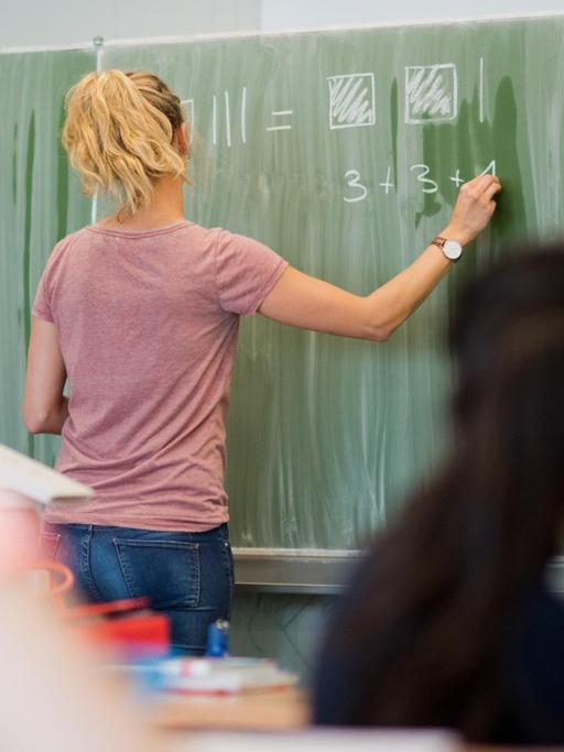 Eine junge Lehrerin schreibt am 17.08.2016 an eine Schultafel im Mathematikunterricht einer 8. Klasse an einer Integrierten Gesamtschule in Hannover (Niedersachsen).