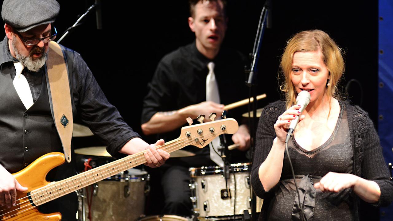 Kitty Hoff singt auf der Bühne des Theaterkahns in Dresden, links von ihr ein Schlagzeuger und ein Bassist.