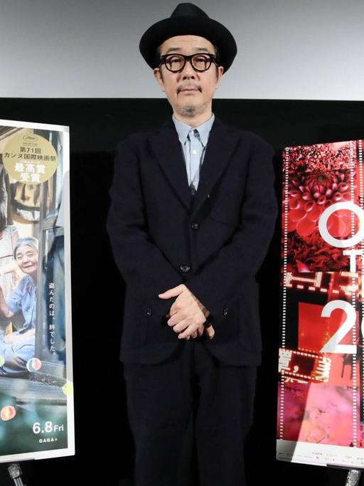 Darsteller Lily Franky beim Tokyo Filmfestival, während der Vorstellung des Films "Shoplifters". Er steht neben einem Filmplakat.