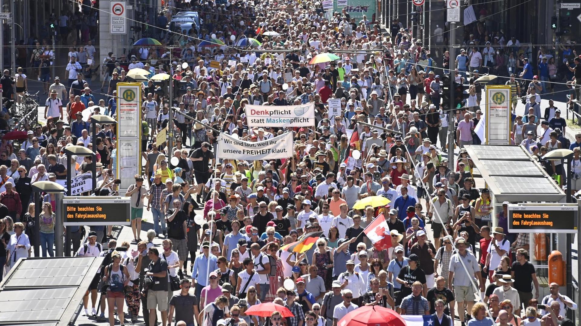 Eine Menschenmenge zieht durch eine Straße, auf einem Transparent steht: "Denkpflicht statt Maskenpflicht"