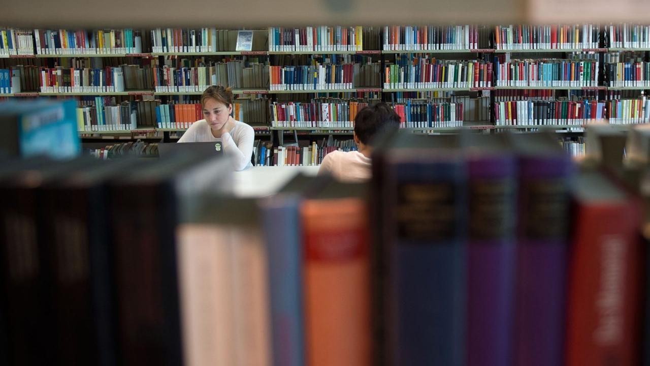 Besucher der Amerika-Gedenkbibliothek in Berlin sitzen zwischen Bücherregalen. 