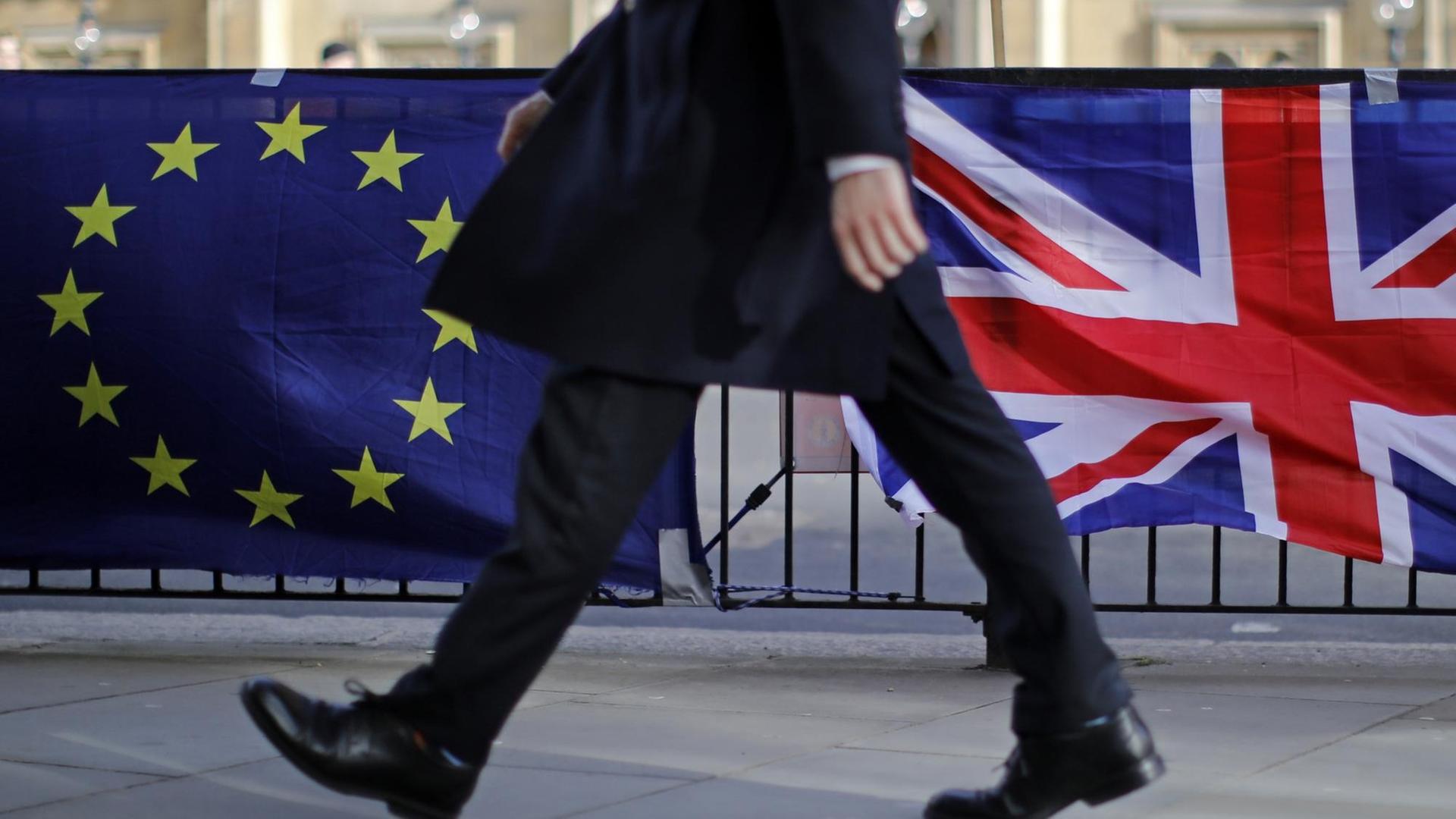 Ein Mann geht vor dem Parlament in London an Flaggen der EU und Großbritanniens vorbei