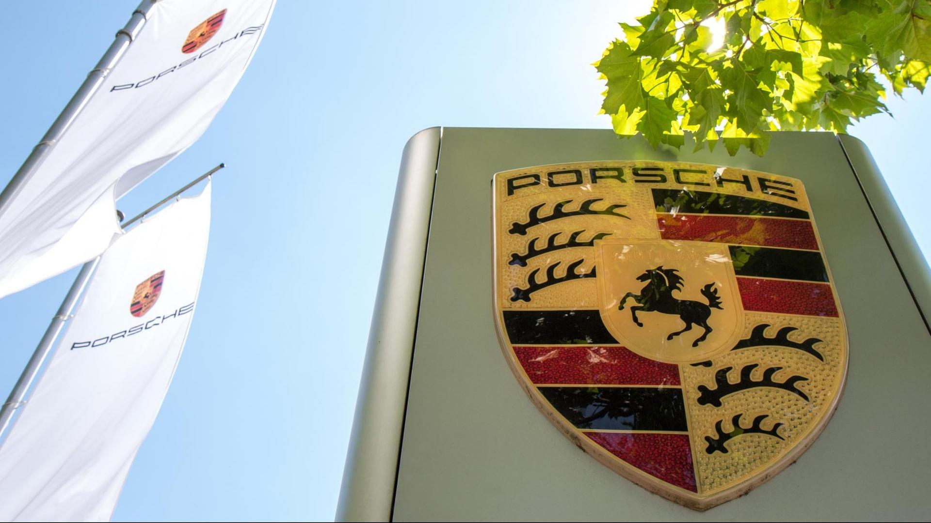 Vor der Konzernzentrale der Porsche AG steht ein gro0es, metallisch glänzendes Logo der Auto-Herstellers. Dahinter sind weiße Fahnen mit dem "Porsche"-Schriftzug zu sehen. Vor der Konzernzentrale der Porsche AG steht ein gro0es, metallisch glänzendes Logo der Auto-Herstellers. Dahinter sind weiße Fahnen mit dem "Porsche"-Schriftzug zu sehen.