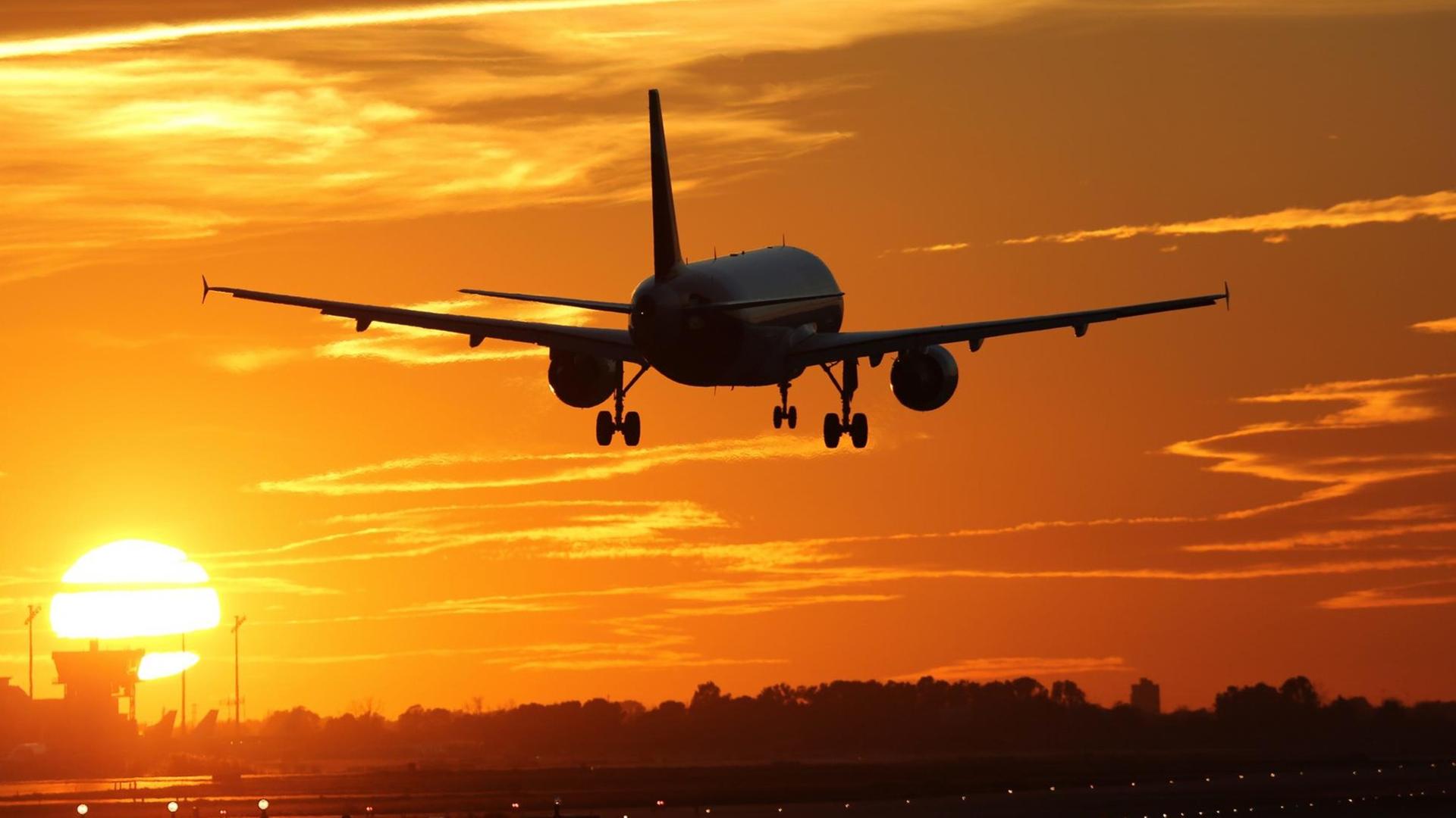 Ein Flugzeug beim Landen auf einem Flughafen mit Sonnenuntergang im Hintergrund.