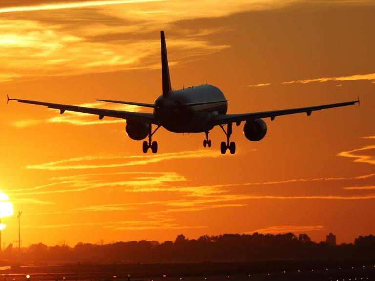 Ein Flugzeug beim Landen auf einem Flughafen mit Sonnenuntergang im Hintergrund.