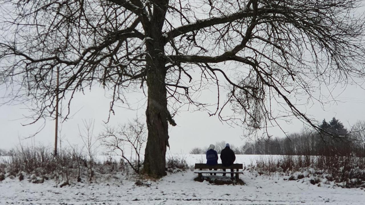 Ein Paar sitzt bei einem Spaziergang im Winter auf einer Bank.