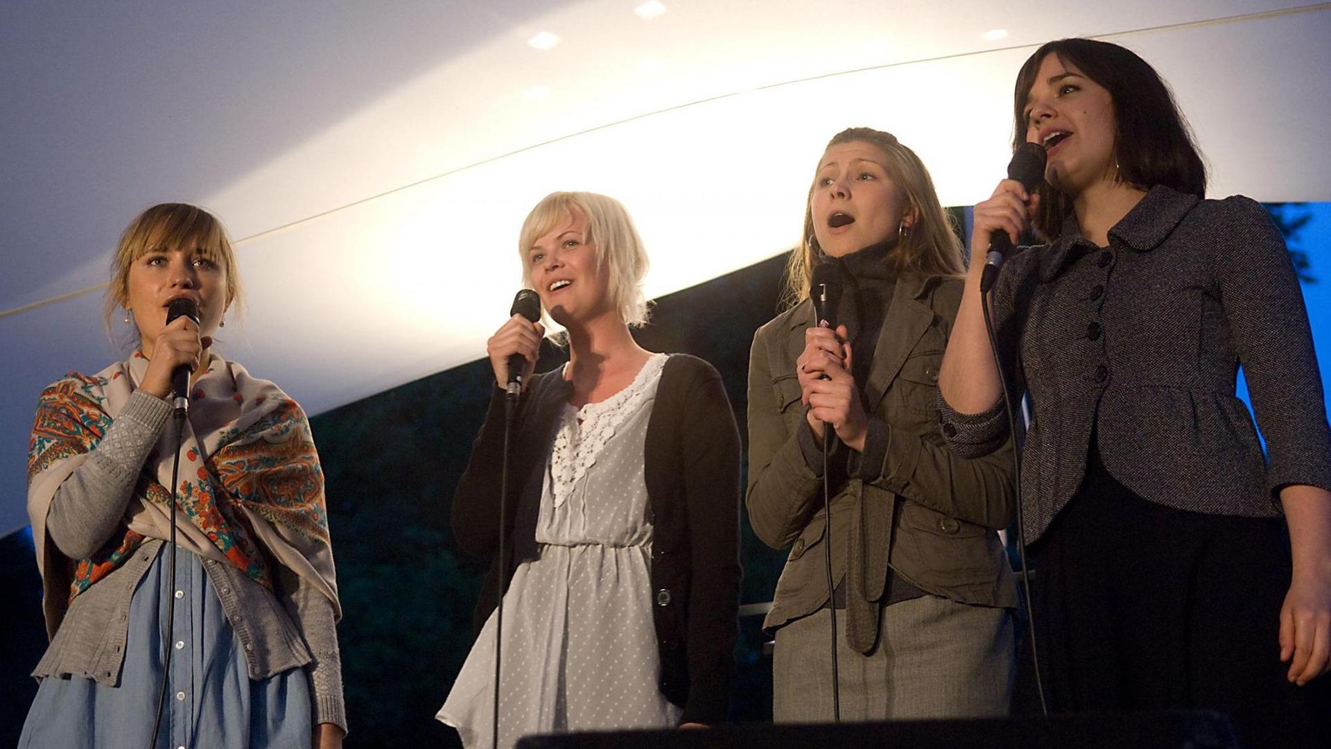 Vier Sängerinnen der Folkband Kraja aus Schweden stehen nebeneinander, halten Mikrofone in der Hand und singen