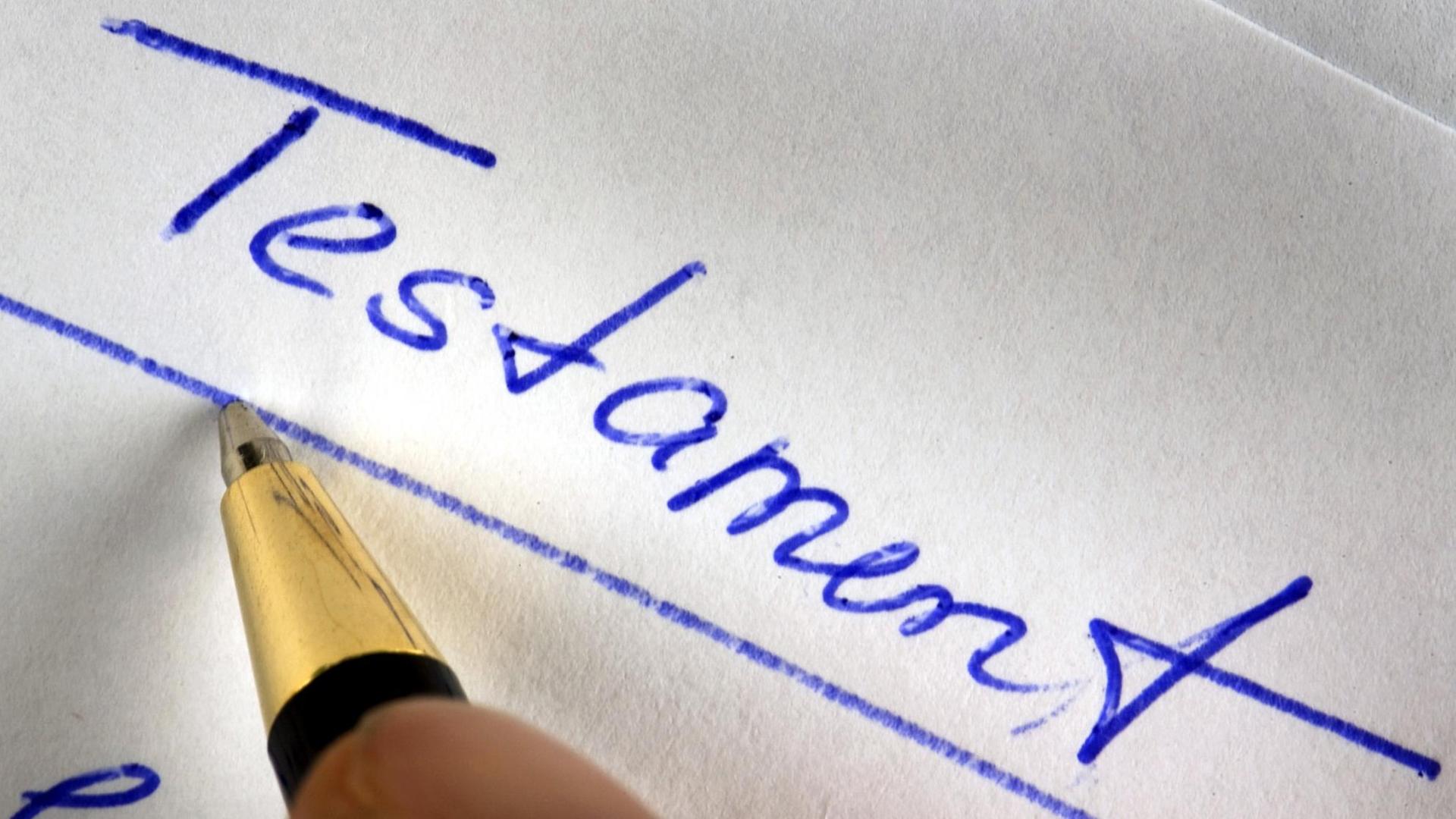 Das Wort Testament wird mit einem Kugelschreiber auf ein Blatt Papier geschrieben.