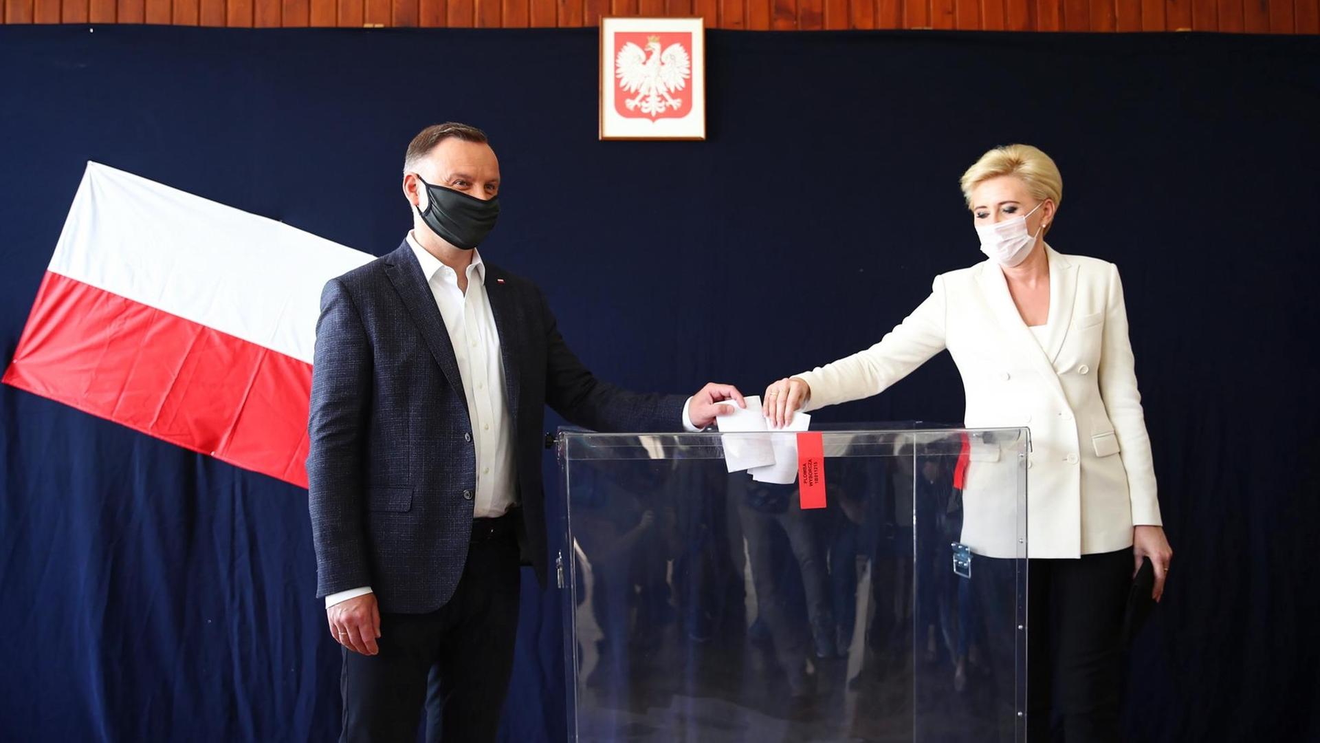 Andrzej Duda, Präsident von Polen und Kandidat für das Amt des Präsidenten der PiS, und seine Frau Agata Kornhauser-Duda. Sie tragen eine Stoffmaske, als sie bei der Präsidentschaftswahl in einem Wahllokal ihre Stimme abgeben.