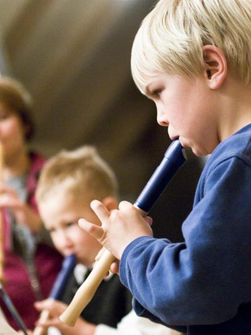 Drei Kinder spielen vor Notenständern auf ihren Blockflöten.