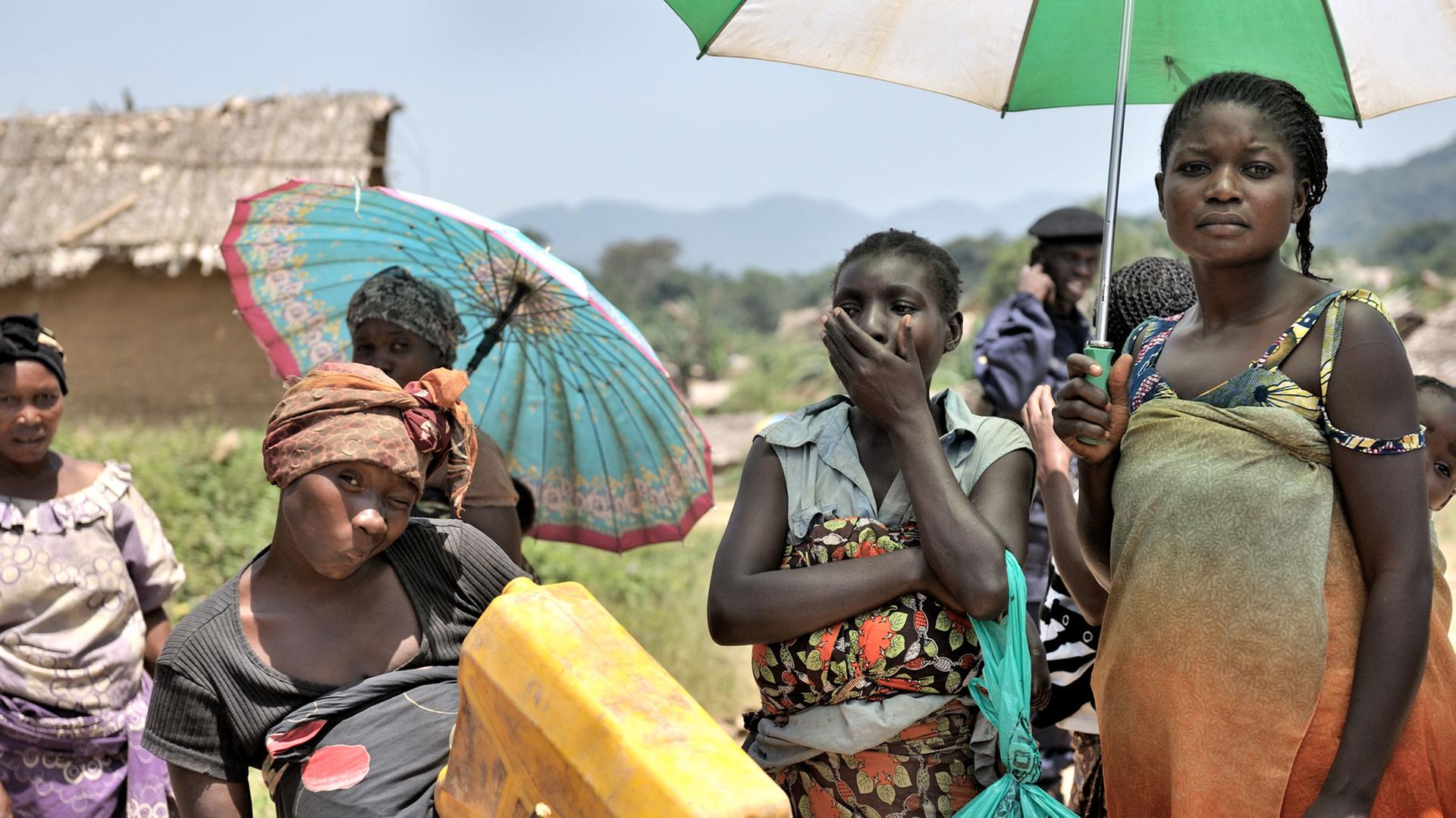 Mehrere Frauen stehen mit Sonnenschirmen in einem Dorf im Ostkongo. Sie wurden 2012 Opfer von Massenvergewaltigungen.
