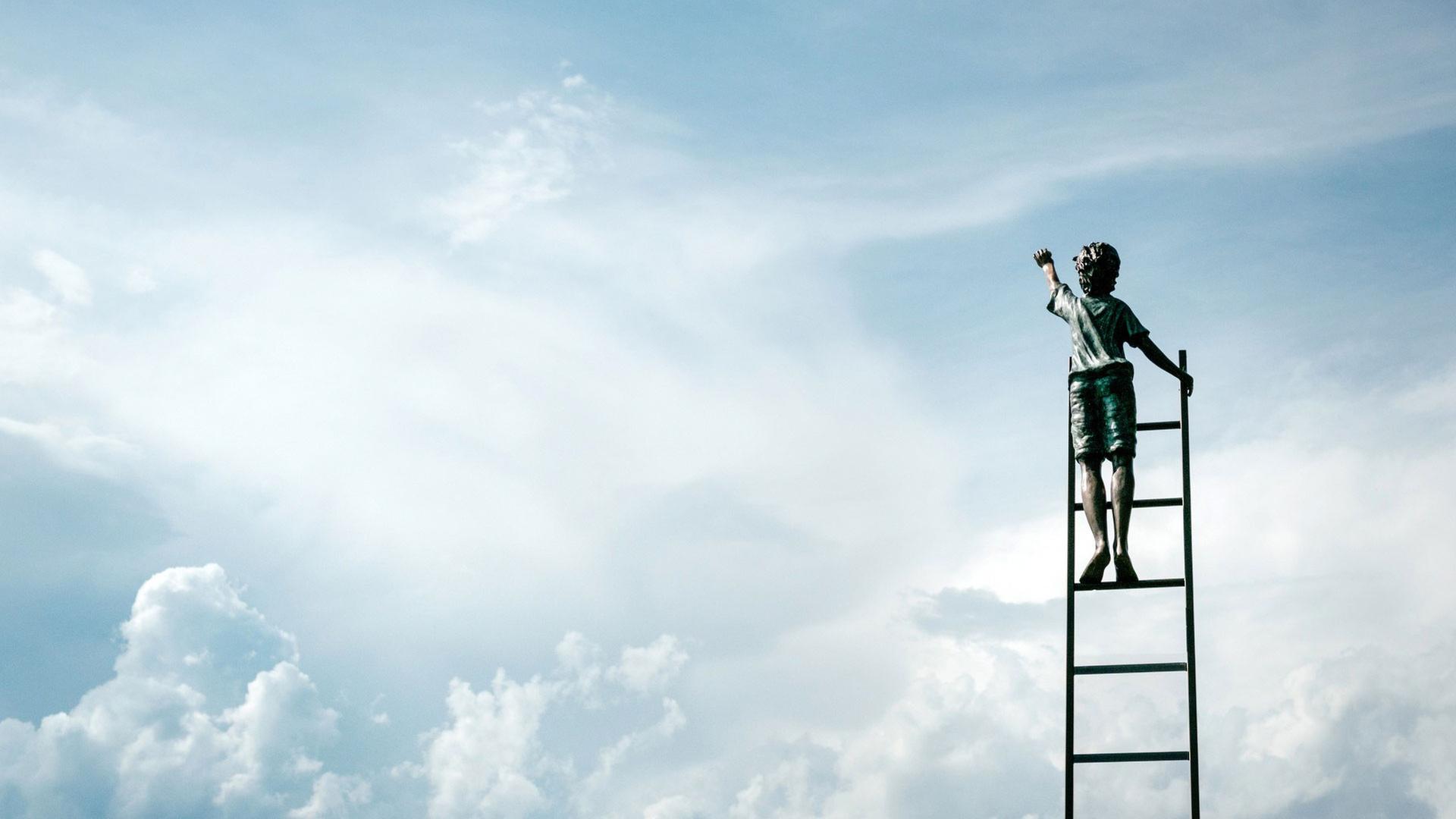 Ein Junge in kurzen Hosen steht auf einer Leiter und streckt die Hand zum Himmel aus.
