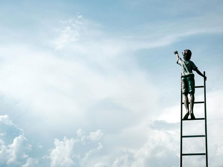 Ein Junge in kurzen Hosen steht auf einer Leiter und streckt die Hand zum Himmel aus.