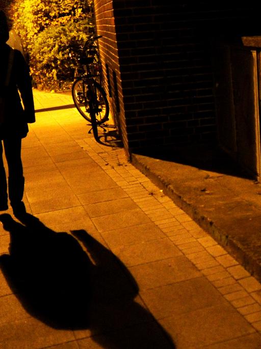 Eine Frau geht im Licht der Straßenlaternen alleine über eine dunkle Straße