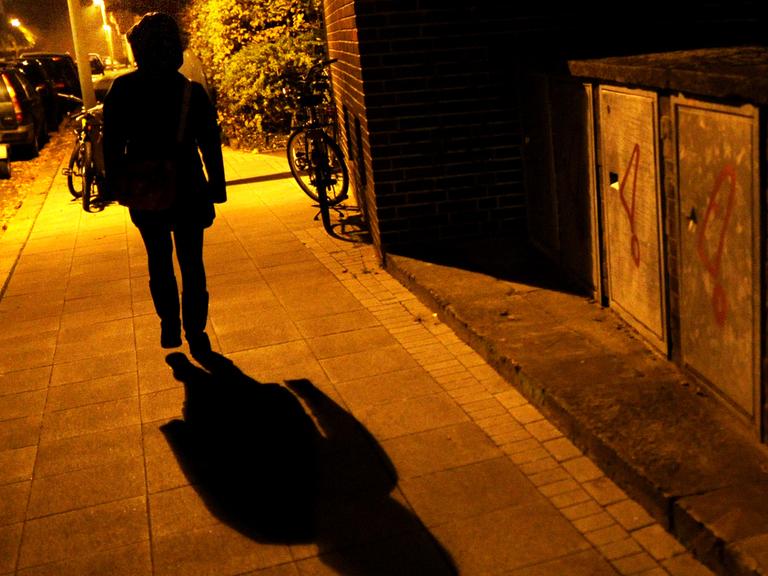 Eine Frau geht im Licht der Straßenlaternen alleine über eine dunkle Straße