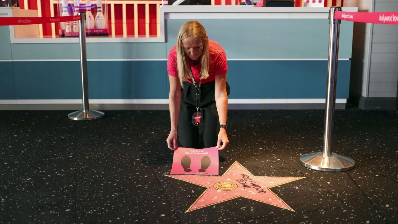 Eine blonde Frau beugt sich über einen rosa Stern und hält ein Plakat mit zwei Fußabdrücken hoch.