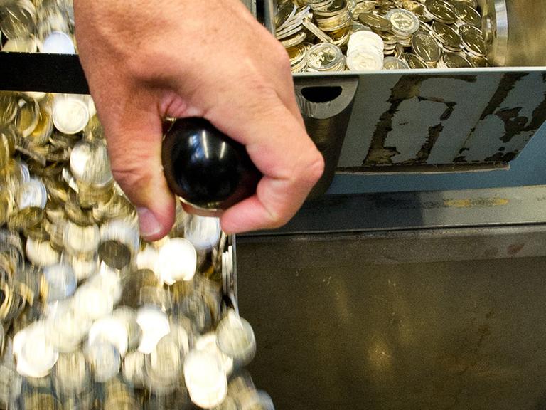 Ein Mann lässt in der staatlichen Münze Baden-Württemberg frisch geprägte Zwei-Euro-Stücke in eine Wanne ab.
