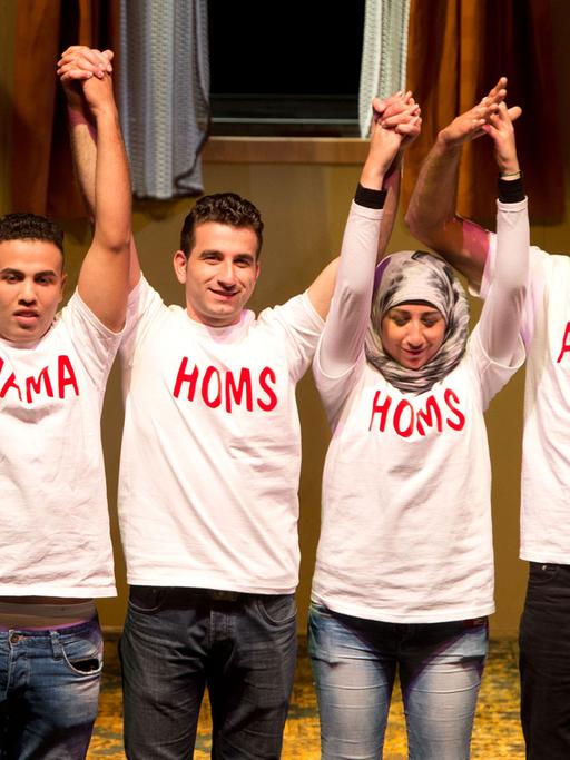Syrische Bürgerkriegsflüchtlinge stehen am 05.10.2014 bei der Premiere der Oper "Cosi fan tutte" auf der Bühne und tragen T-Shirts mit den Namen der Orte ihrer Herkunft.