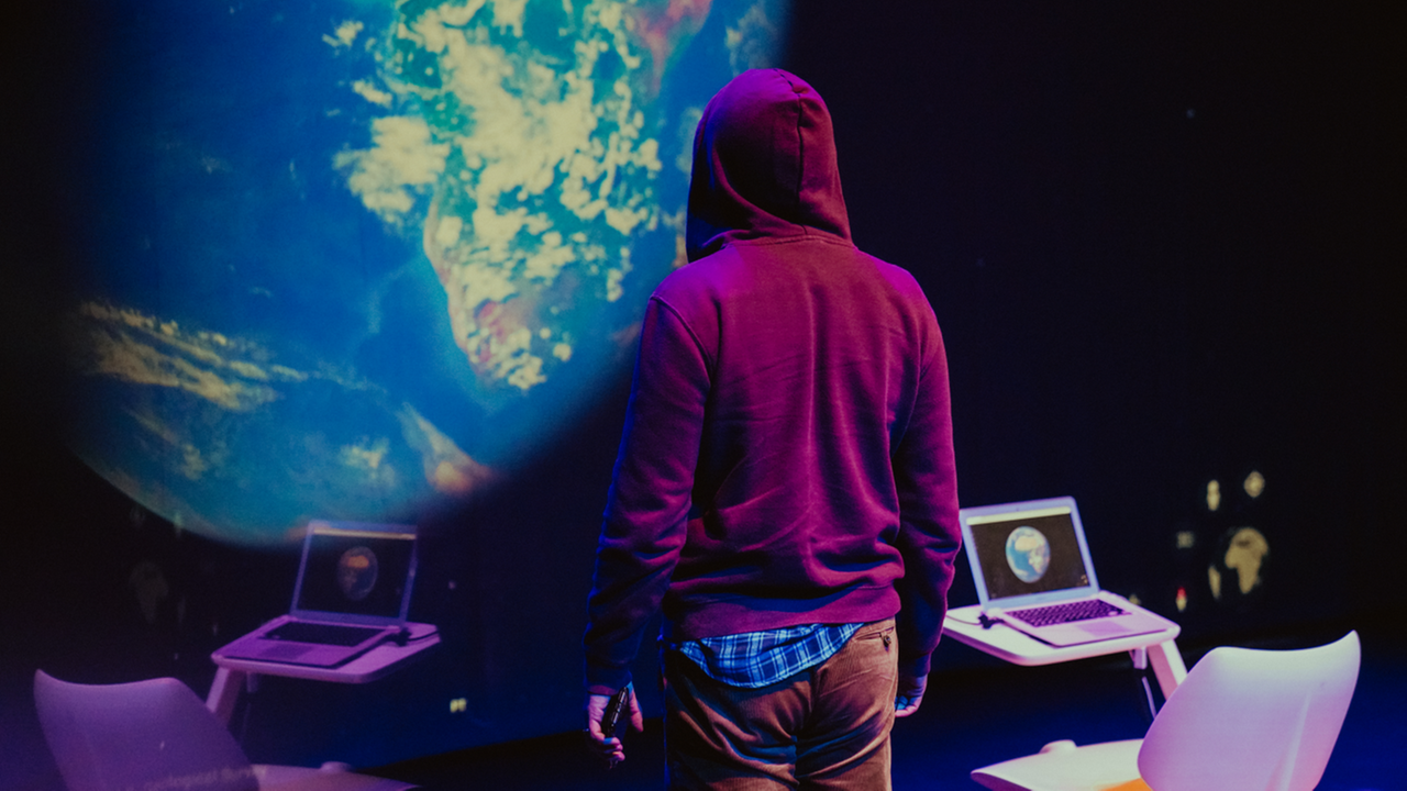 Ansicht der Installation von Ana-Viotti, vor einer Weltkugel stehen eine Person und zwei Laptops.