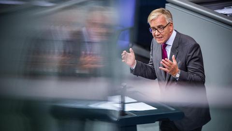 Bartsch spricht und gestikuliert am Rednerpult, er spiegelt sich dabei undeutlich in einer Scheibe.