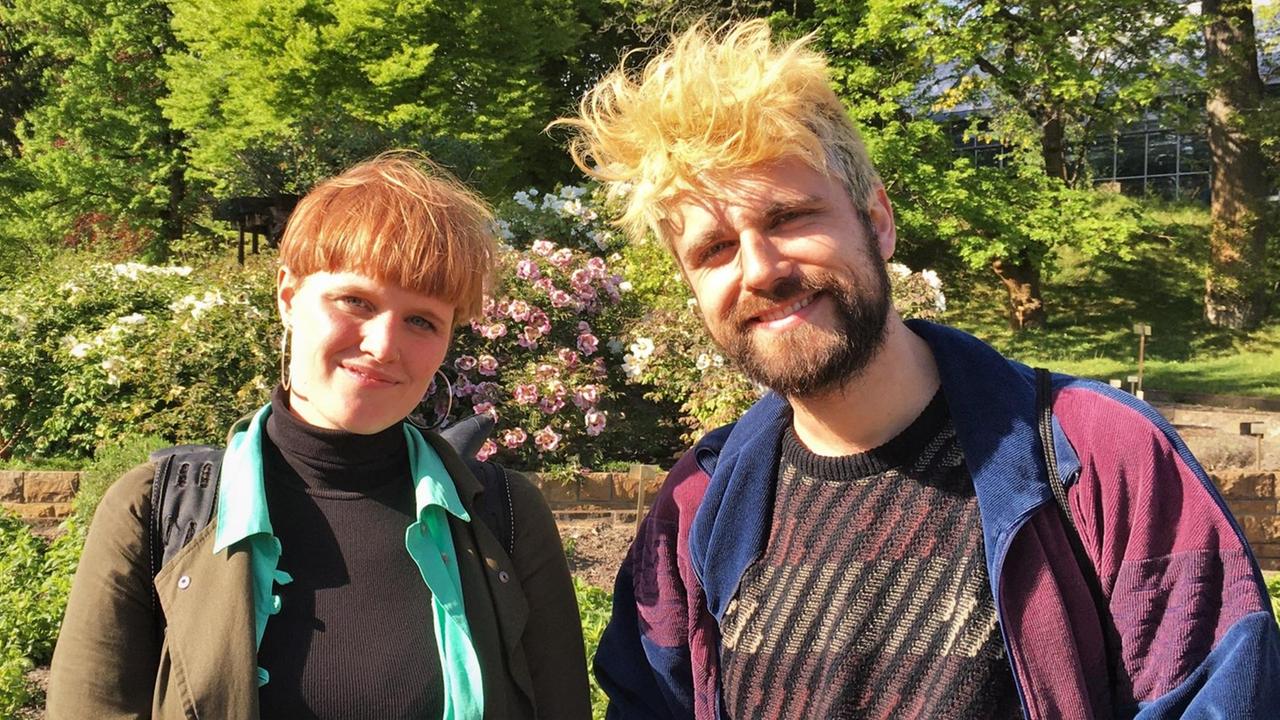 Eva Schimmelmann und Florian Sonntag stehen im Botanischen Garten und blicken direkt in die Kamera.