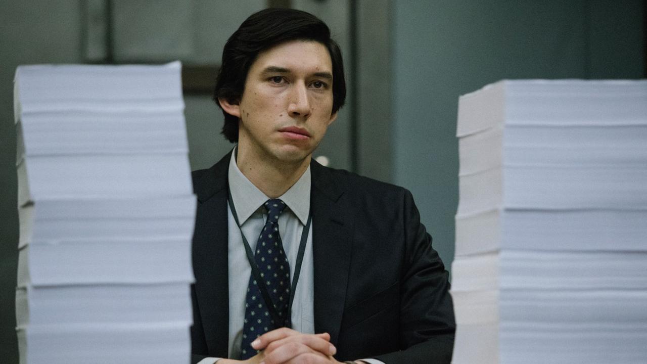 Adam Driver als Senatsmitarbeiter Daniel Jones sitzt vor hinter hohen Papierstapeln an seinem Schreibtisch.