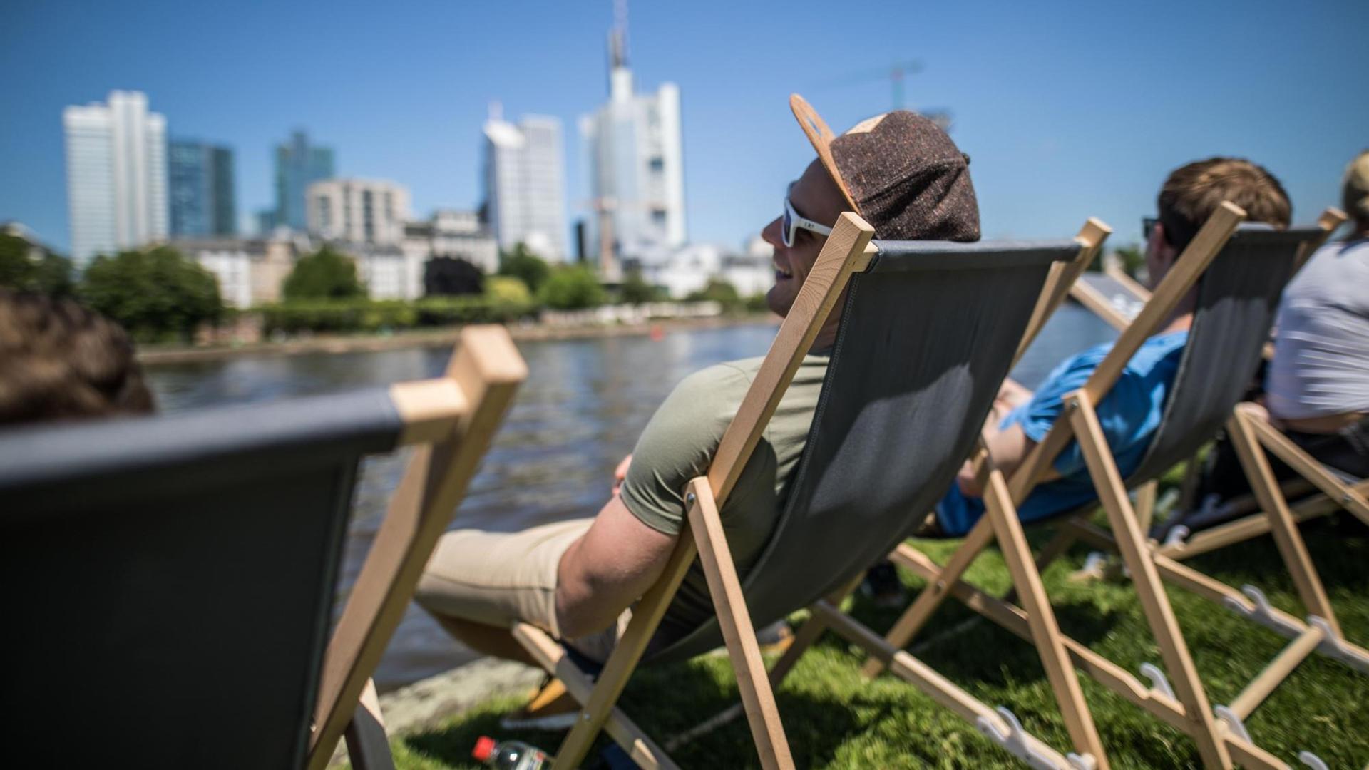 Junge Männer sitzen in Liegestühlen am Mainufer