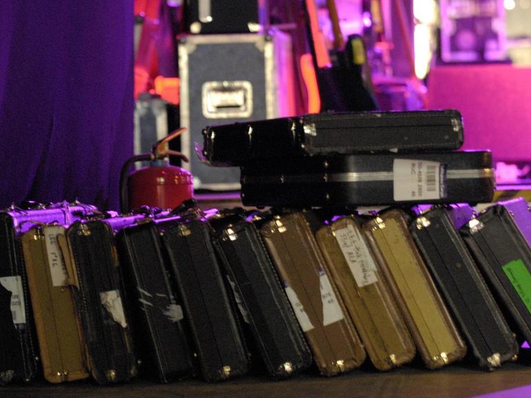Gitarrenkoffer liegen nebeneinander vor einer hell erleuchteten Bühne.
