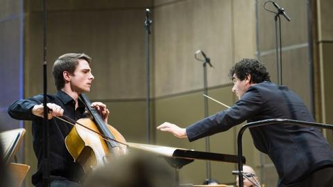 Der Cellist spielt auf seinem Instrument, neben ihm ist der Dirigent in Aktion zu sehen.