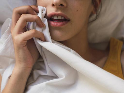 Eine junge Frau liegt in einem Bett und hält ein Laken.