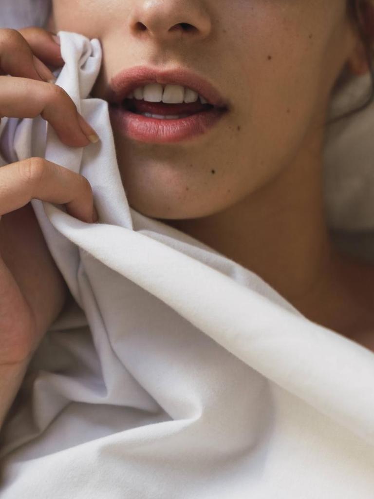 Eine junge Frau liegt in einem Bett und hält ein Laken.