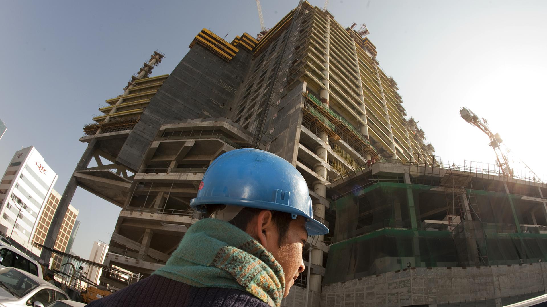 Ein asiatischer Arbeiter mit blauem Schutzhelm steht auf einer Baustelle in Doha.