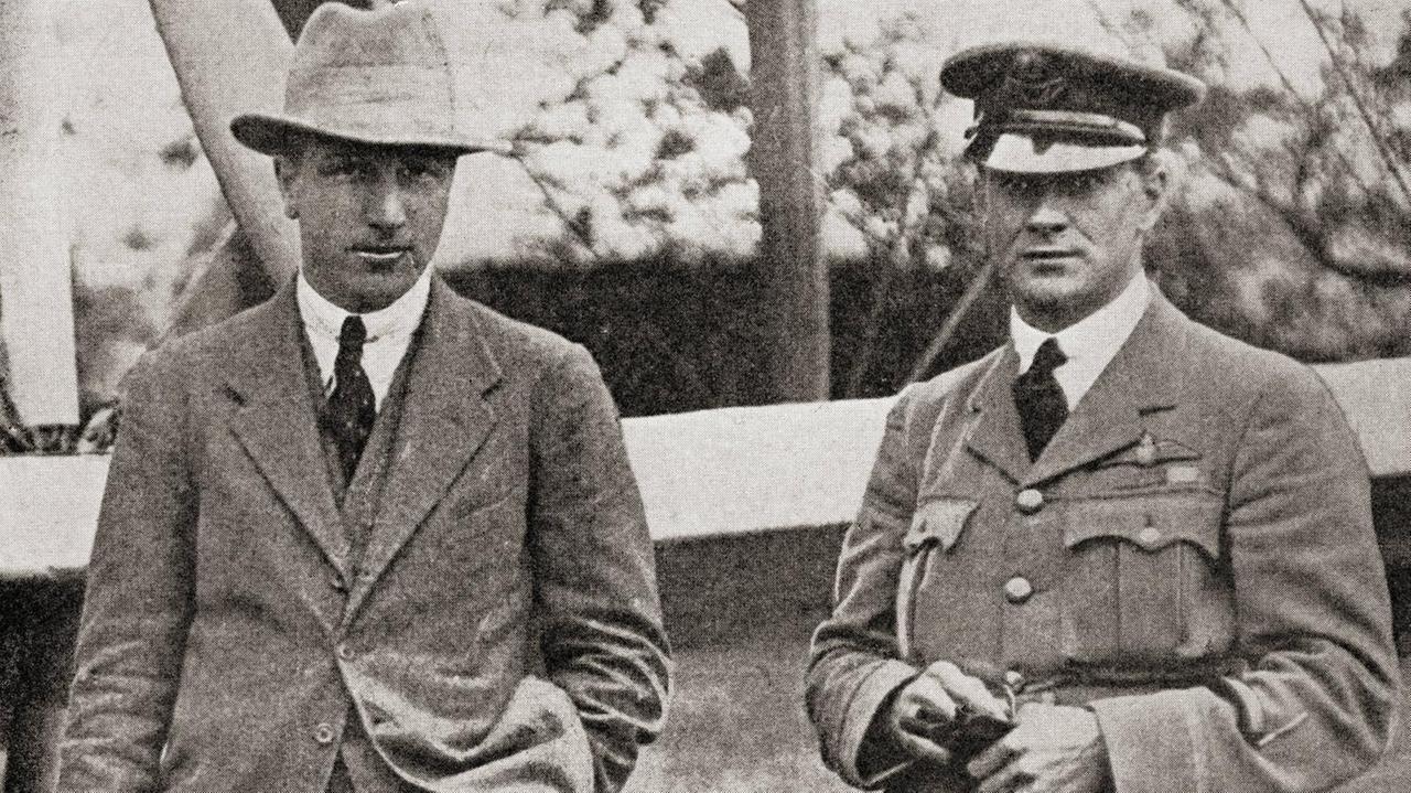 John Alcock (links) und Arthur Brown stehen vor einem Flugzeug und schauen in die Kamera.